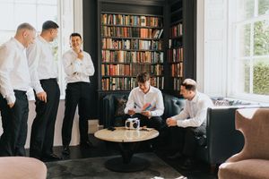 A group in formal white shirts gather around a round table in a room with floor-to-ceiling bookshelves at Saltmarshe Hall.