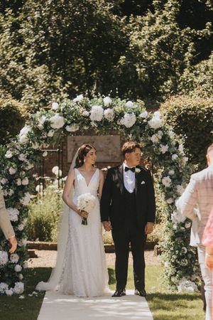 A romantic garden wedding ceremony features a floral arch adorned with white roses and greenery at Saltmarshe Hall.