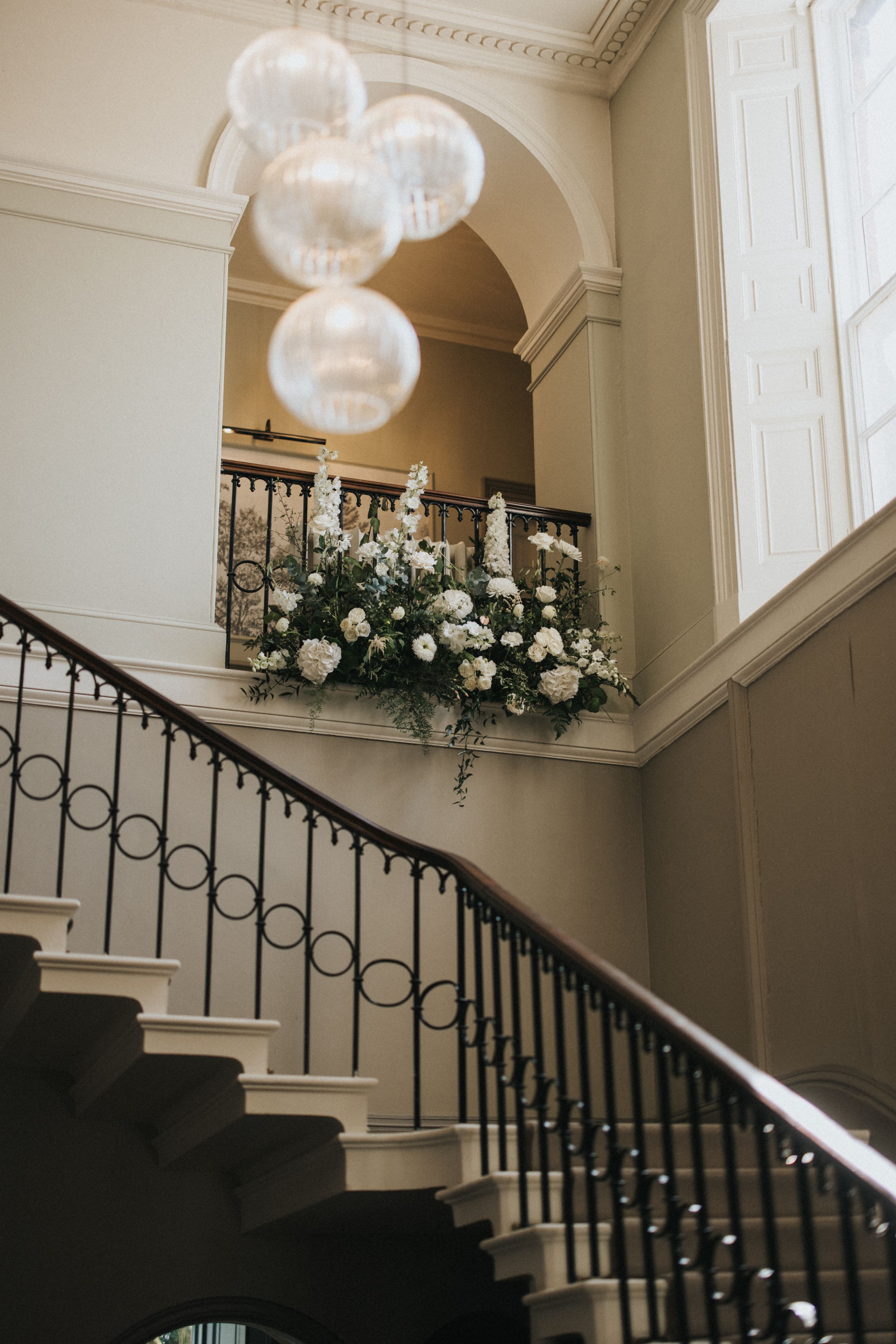 Elegant white staircase with black iron railings, decorated with crystal chandeliers and floral arrangements at Saltmarshe Hall.