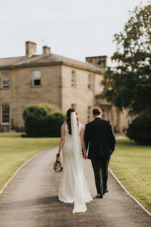 Bride and groom walking down path together at Saltmarshe Hall with manicured lawn on sunny wedding day - taken by Grimsby photographer.
