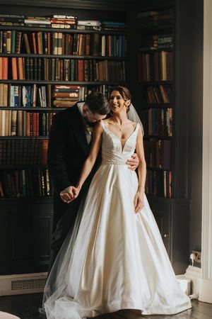 Bride in a flowing white empire waist wedding gown poses with groom in front of library bookshelves at Saltmarshe Hall.
