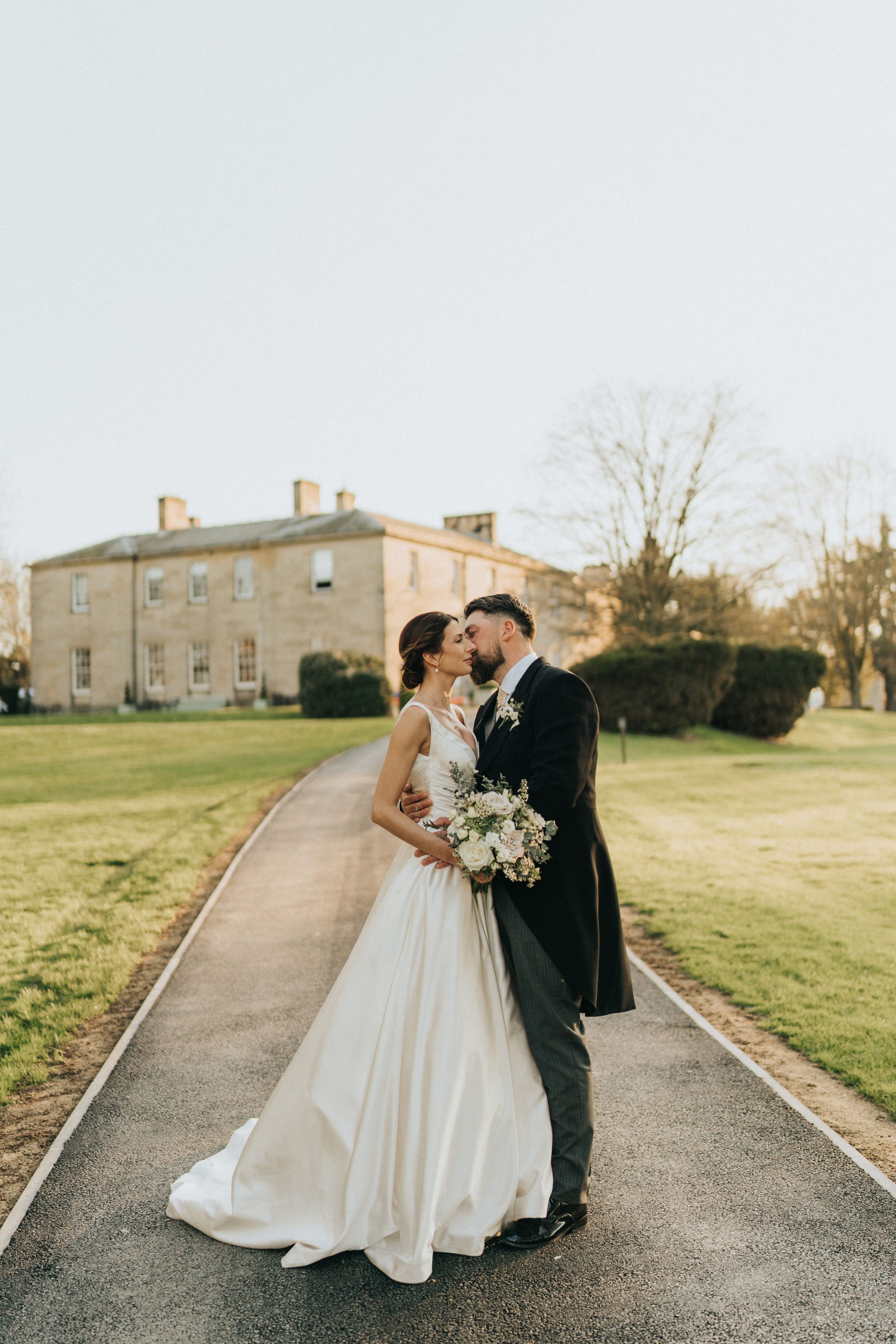 A wedding couple embraces on a pathway in front of Saltmarshe Hall - taken by Grimsby photographer.