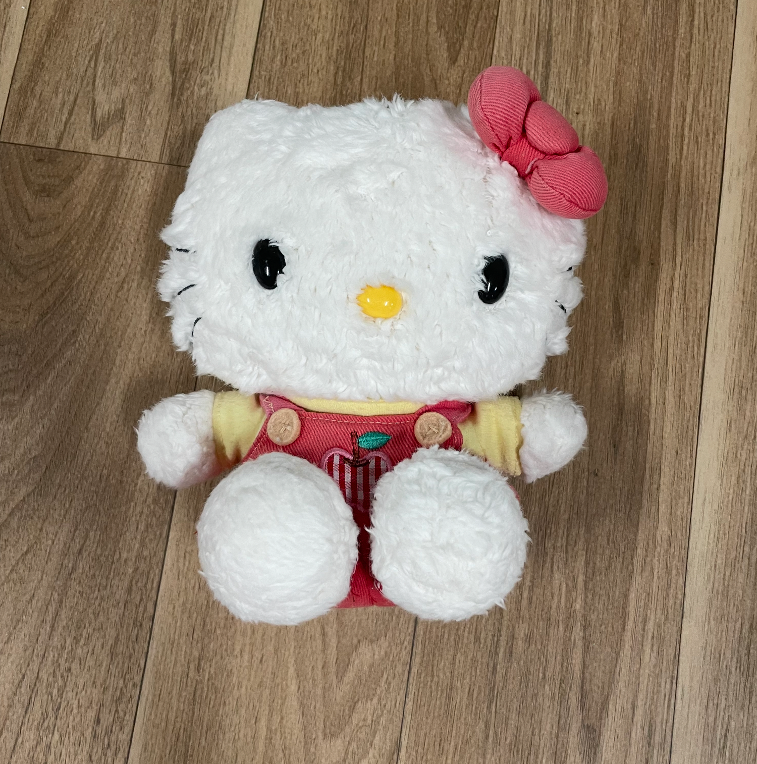 White plush Hello Kitty toys with pink bows displayed on hardwood flooring.