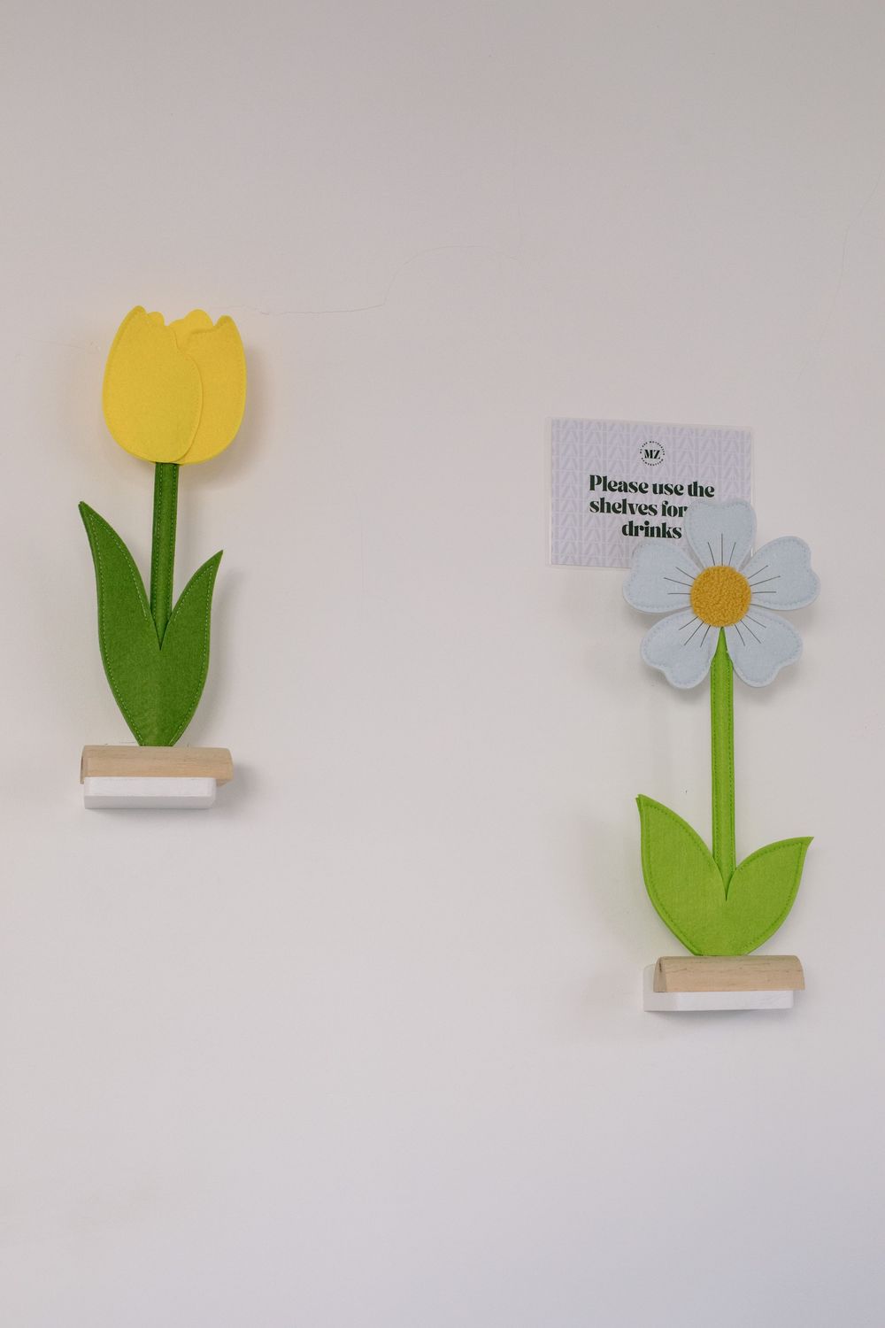 Two decorative wall-mounted flowers, a yellow tulip and white daisy with green stems and small signs.