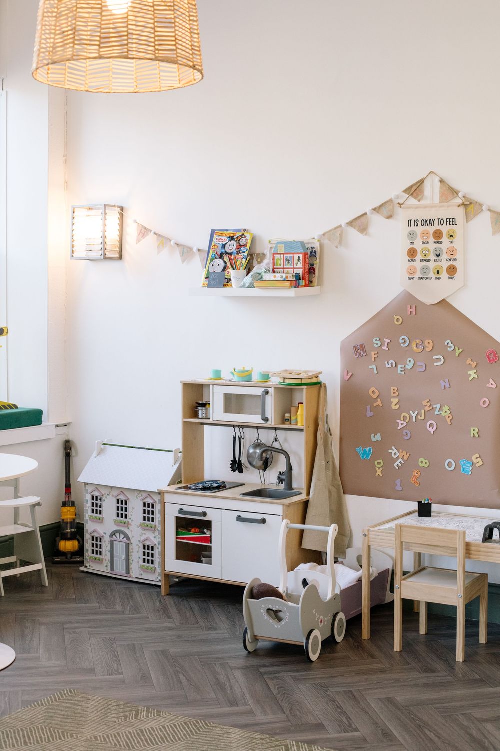Cozy children's play area with toy kitchen, doll house, and educational decorations in a modern minimalist room setting.