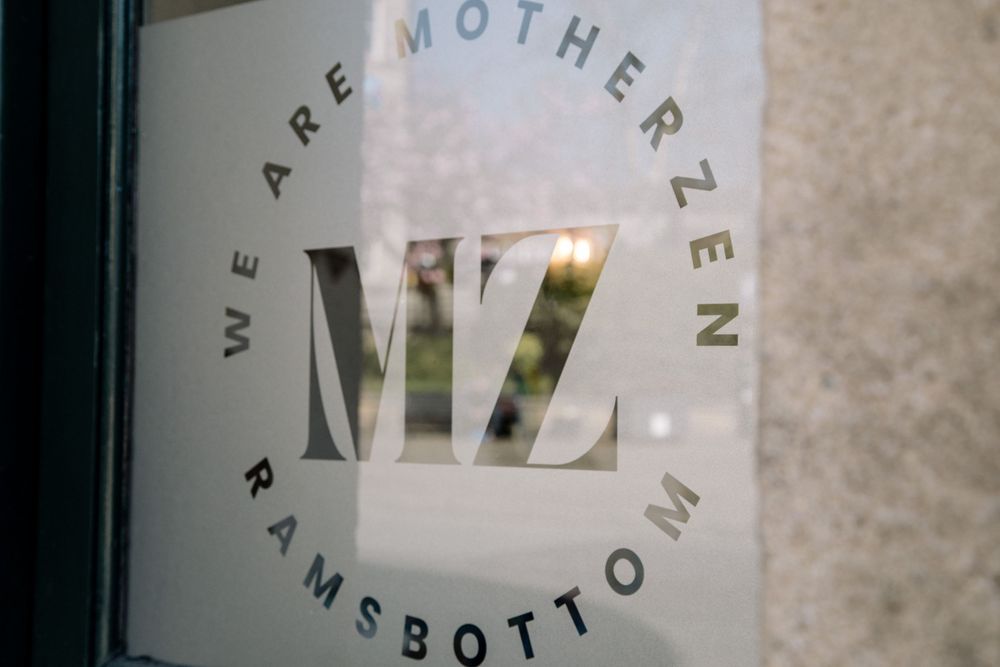 A storefront window with 'We are Motherzen' text printed in elegant typography.
