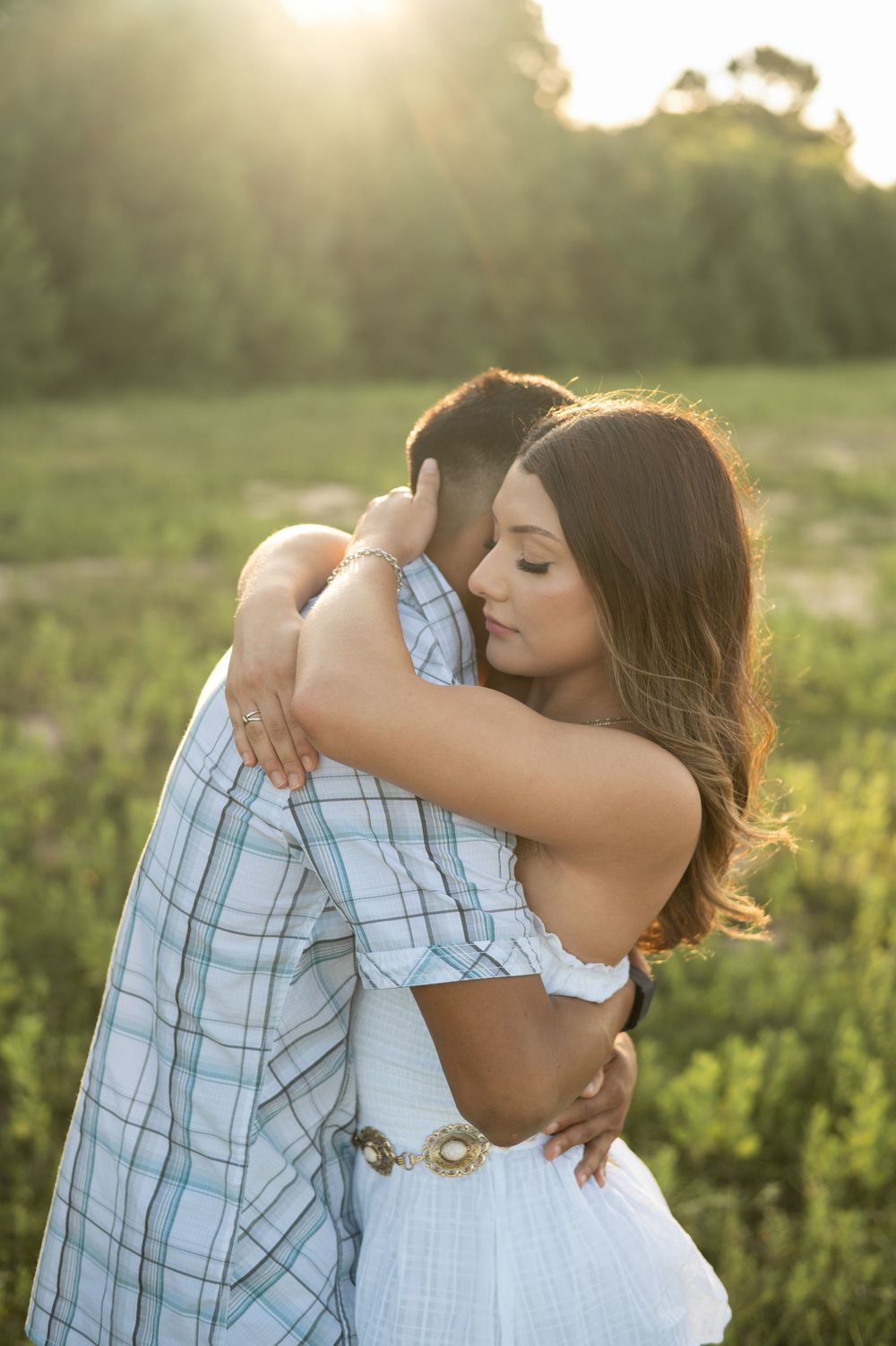 Two people embrace in a loving hug against a golden sunset in a grassy field, creating a romantic silhouette.