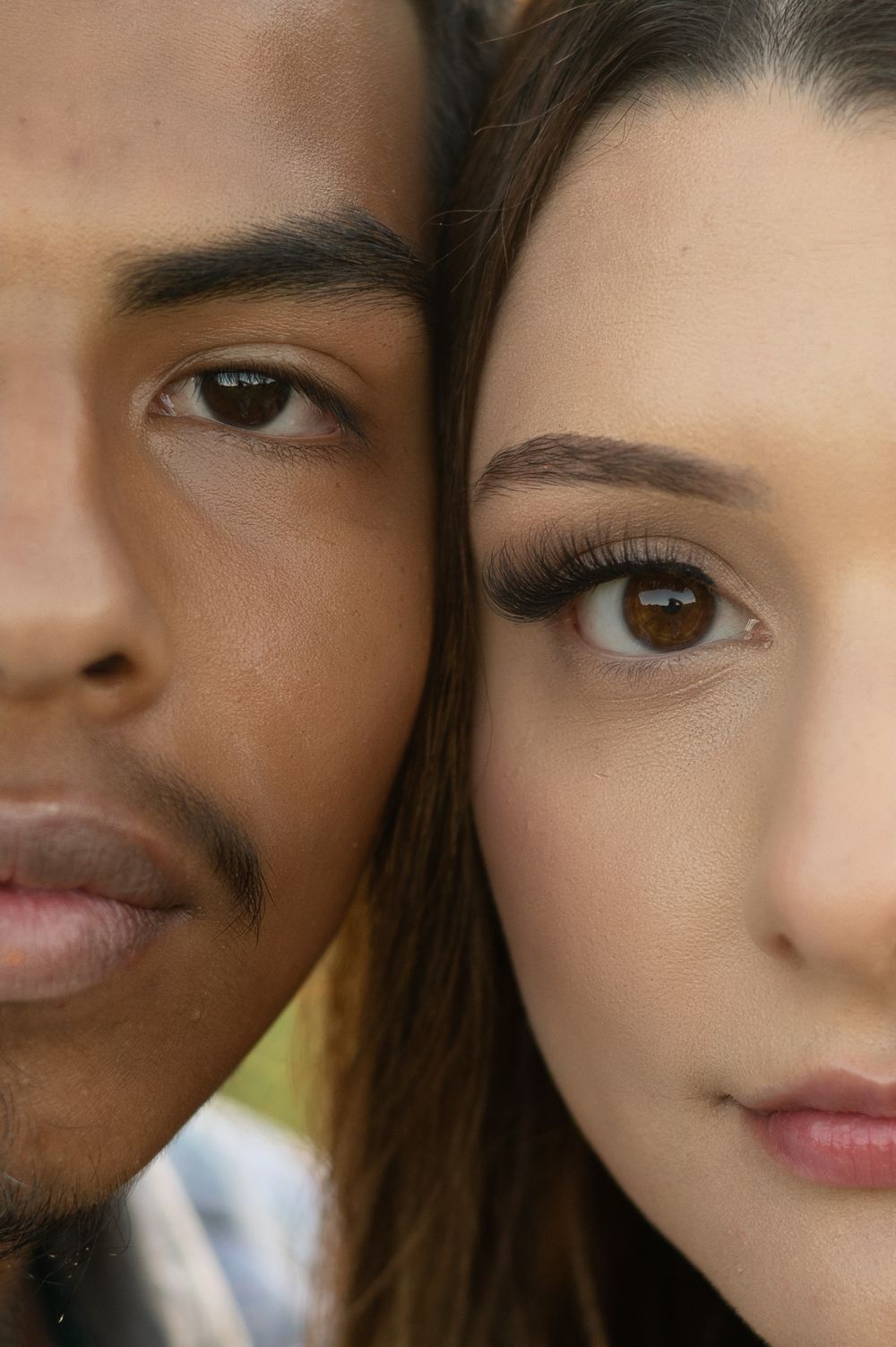 Close-up portrait showing two faces side by side with contrasting skin tones and brown eyes looking at camera.
