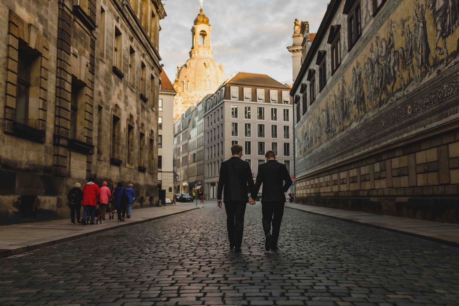 Historic cobblestone street in Dresden shows the famous Fürstenzug mural along an ancient city wall at sunset.