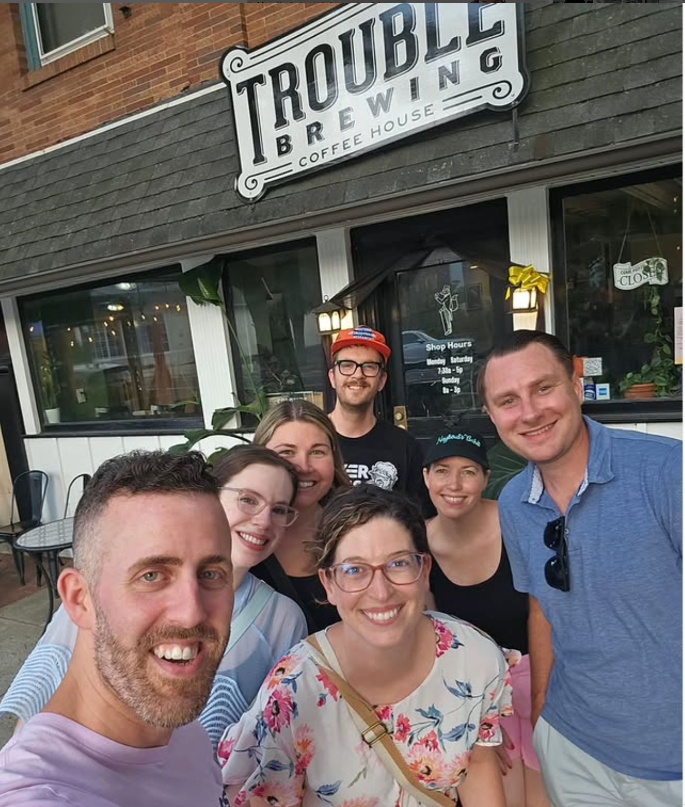 A group poses together outside Trouble Brewing establishment with a black exterior and white storefront sign.