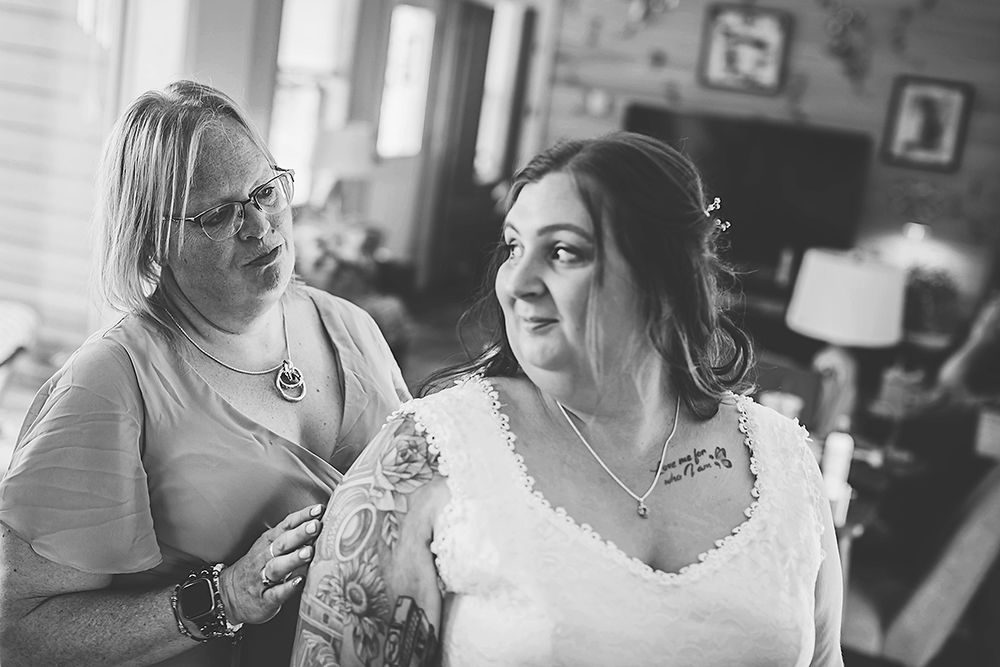 A bride in a white lace wedding dress gets ready with assistance in a cozy home setting.