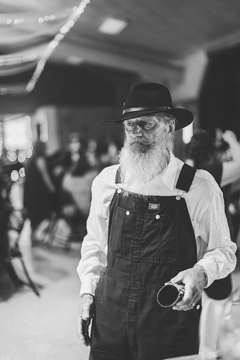 Black and white photo of guest in overalls and hat during wedding reception.