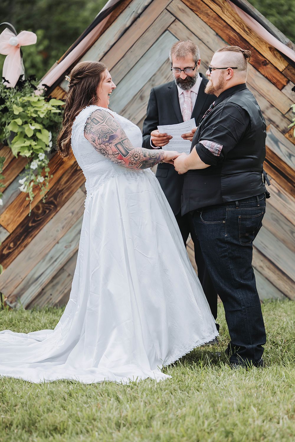Outdoor wedding ceremony with rustic wooden backdrop as couple exchanges vows.