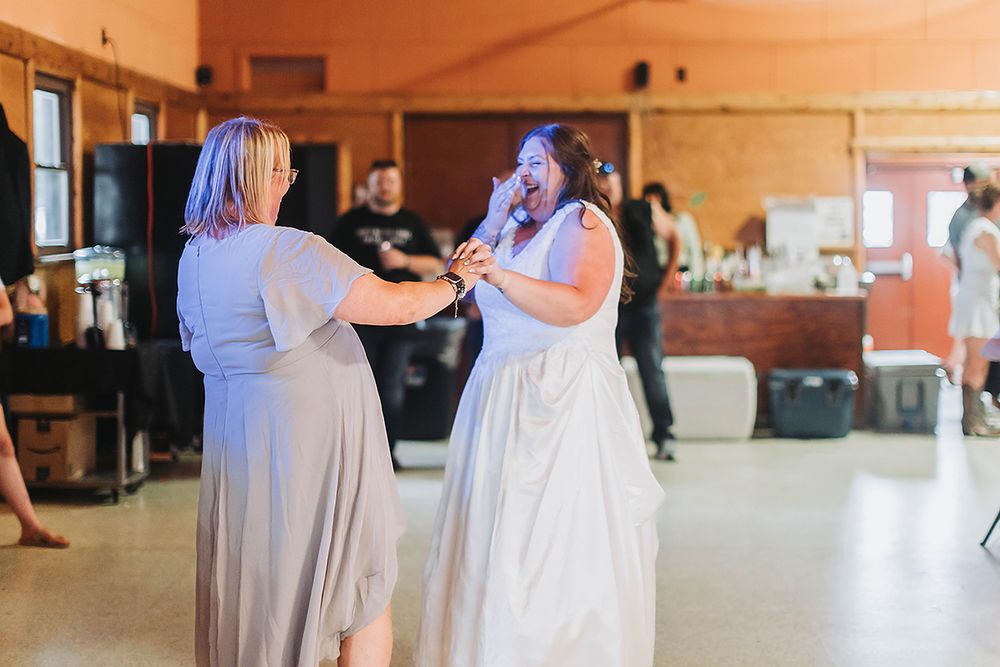 Two people dancing joyfully together in a sunny event space during a wedding celebration.
