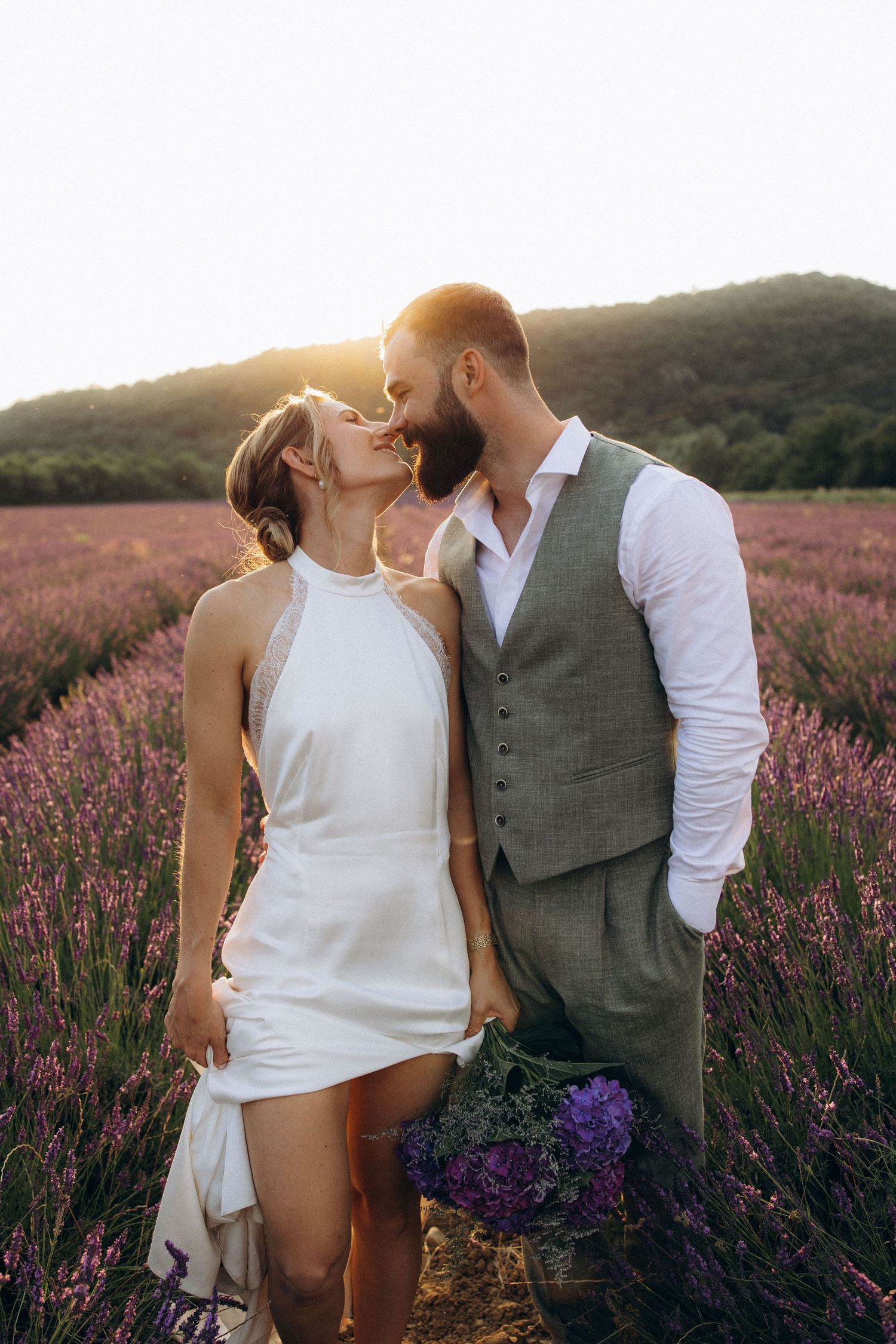 A romantic couple shares an intimate moment in a blooming lavender field at sunset with purple flowers in a basket.