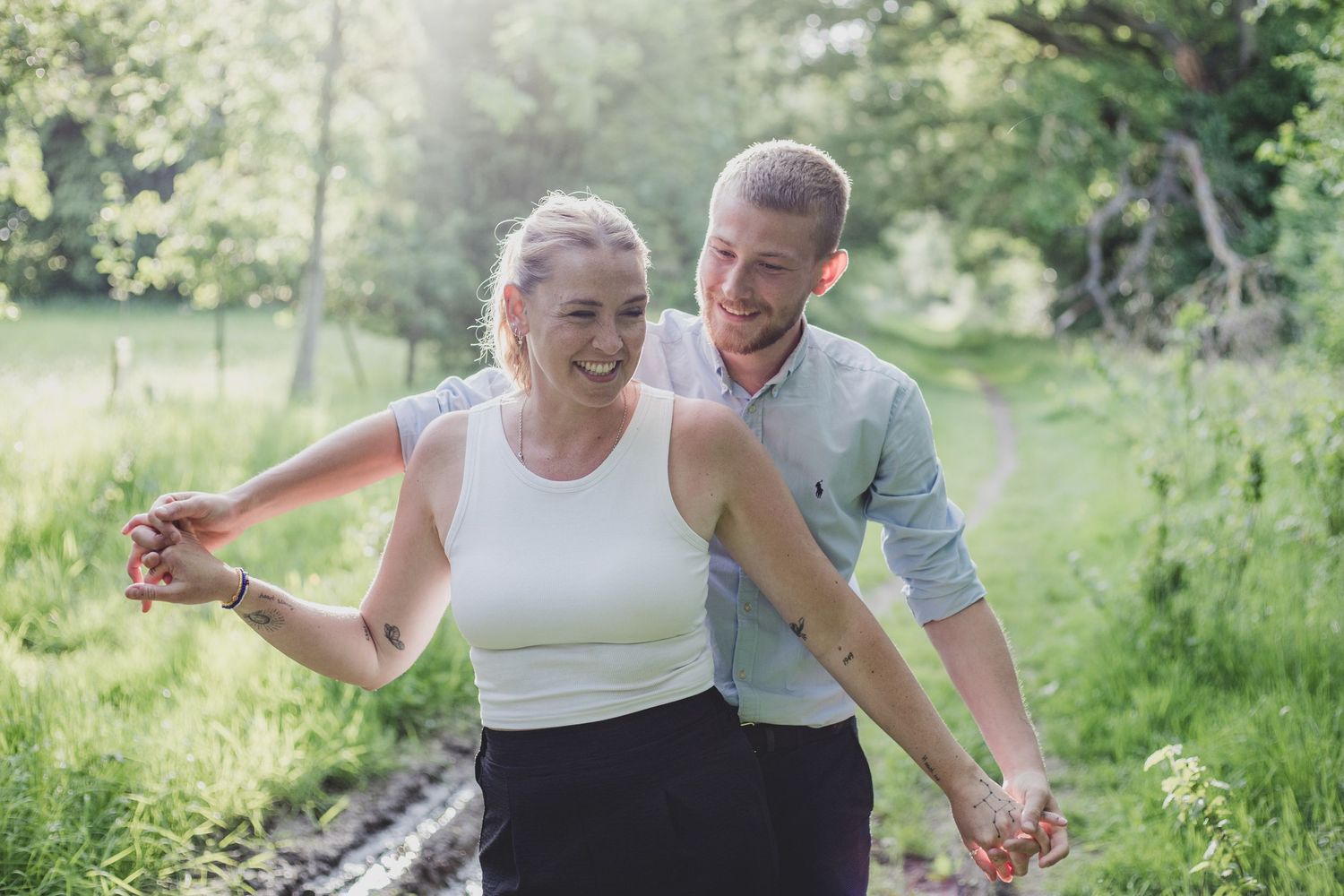 A joyful couple walks together on a winding path through lush green summer meadows while holding hands.