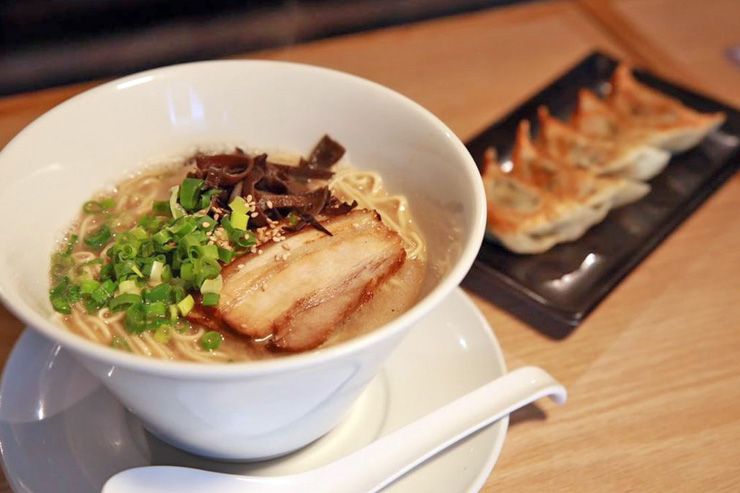 A bowl of ramen noodle soup with sliced pork chashu, green onions and side plate of gyoza dumplings on wooden table.