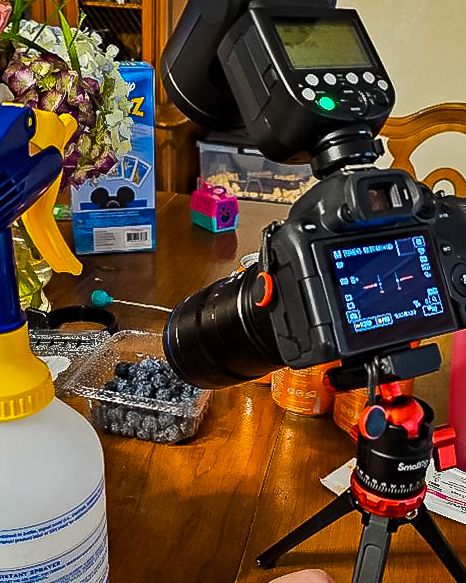 Microscope and camera setup on wooden desk with illuminated digital display in dark room.