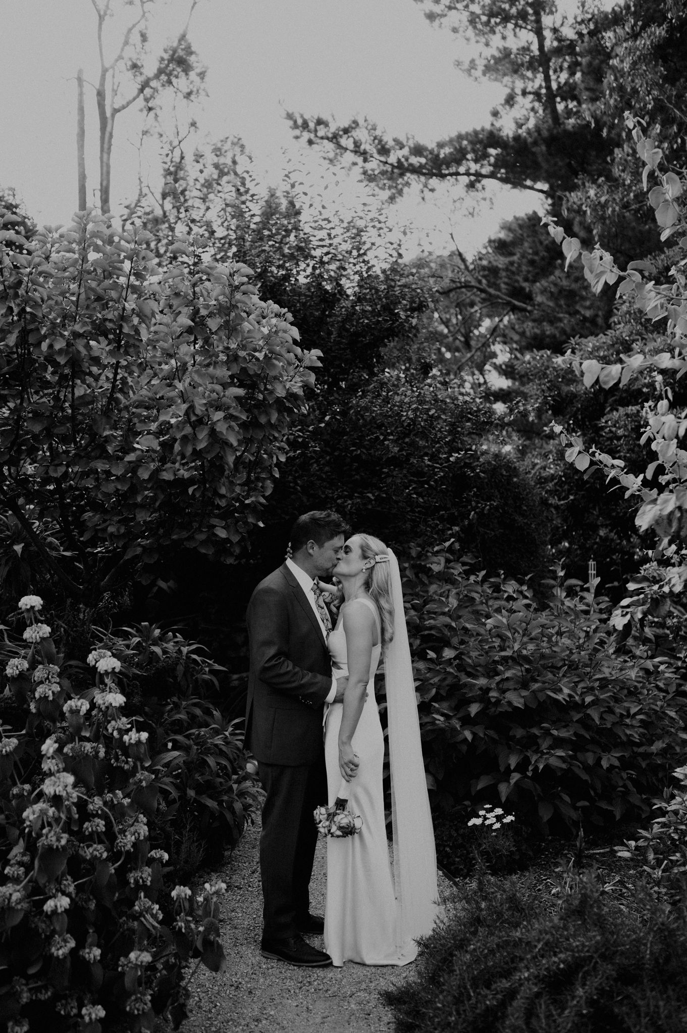 Black and white garden wedding photo surrounded by blooming roses and greenery.