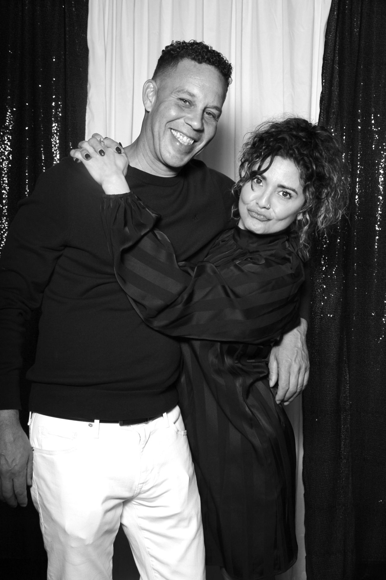 A black and white photo of two people making exaggerated silly faces and poses against a sparkly backdrop.