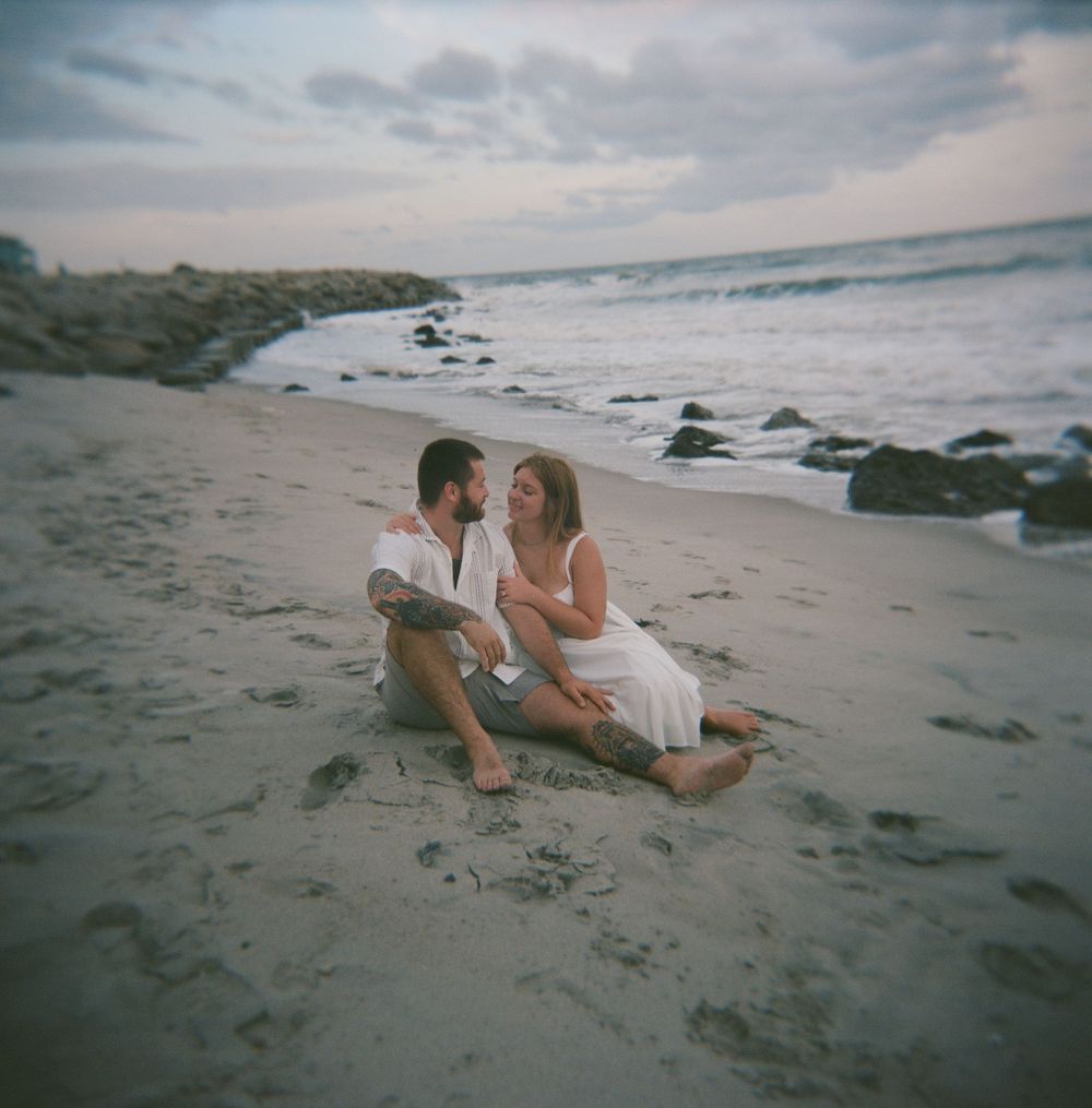 A romantic seaside photoshoot sequence of a couple lounging on a sandy beach at sunset.