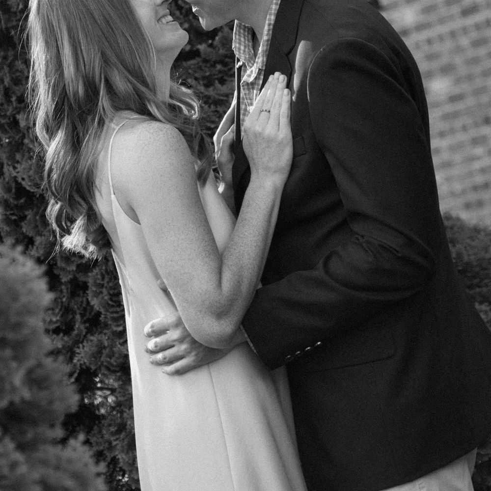 Black and white photo series showing romantic couple embracing in close intimate poses against brick wall backdrop.