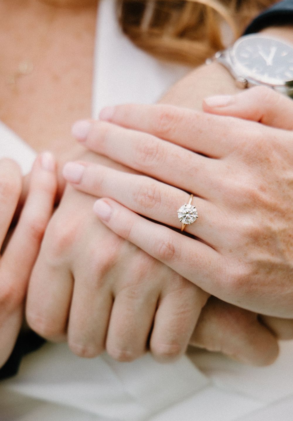 Close-up view of delicate hands displaying a sparkling engagement ring with a soft, romantic blur.