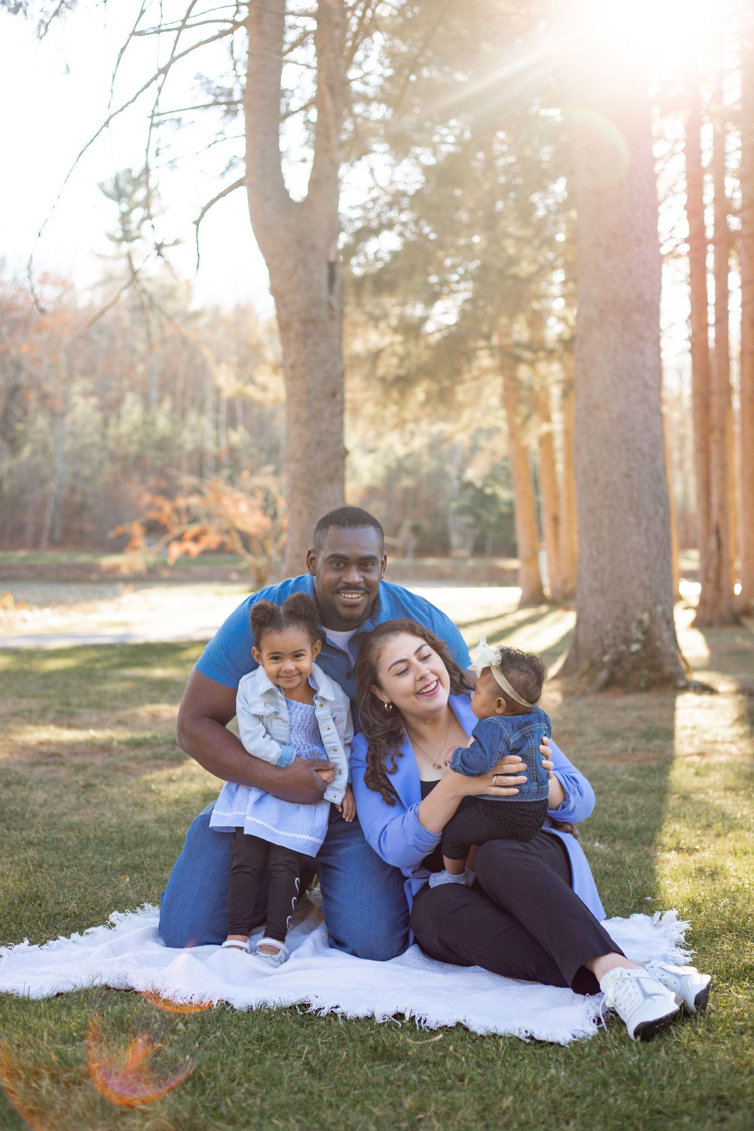 a family siting on a picnic blanket as the the sun shines through the trees
