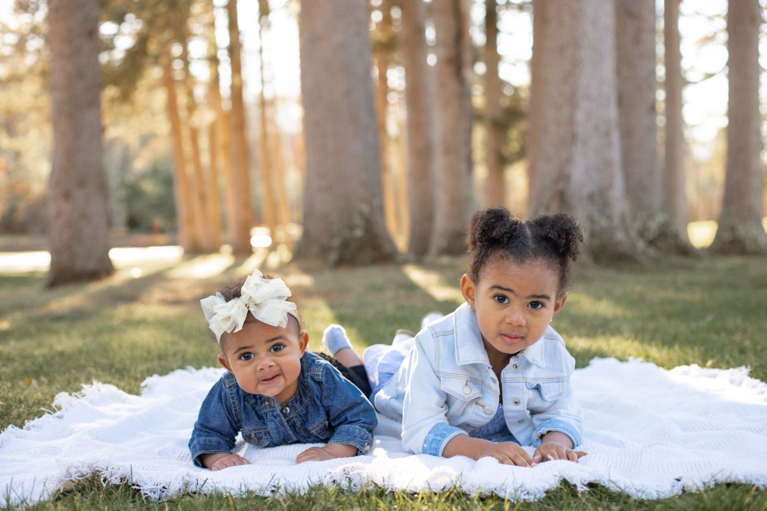 two sisters laying on a picnic blanket as the the sun shines through the trees
