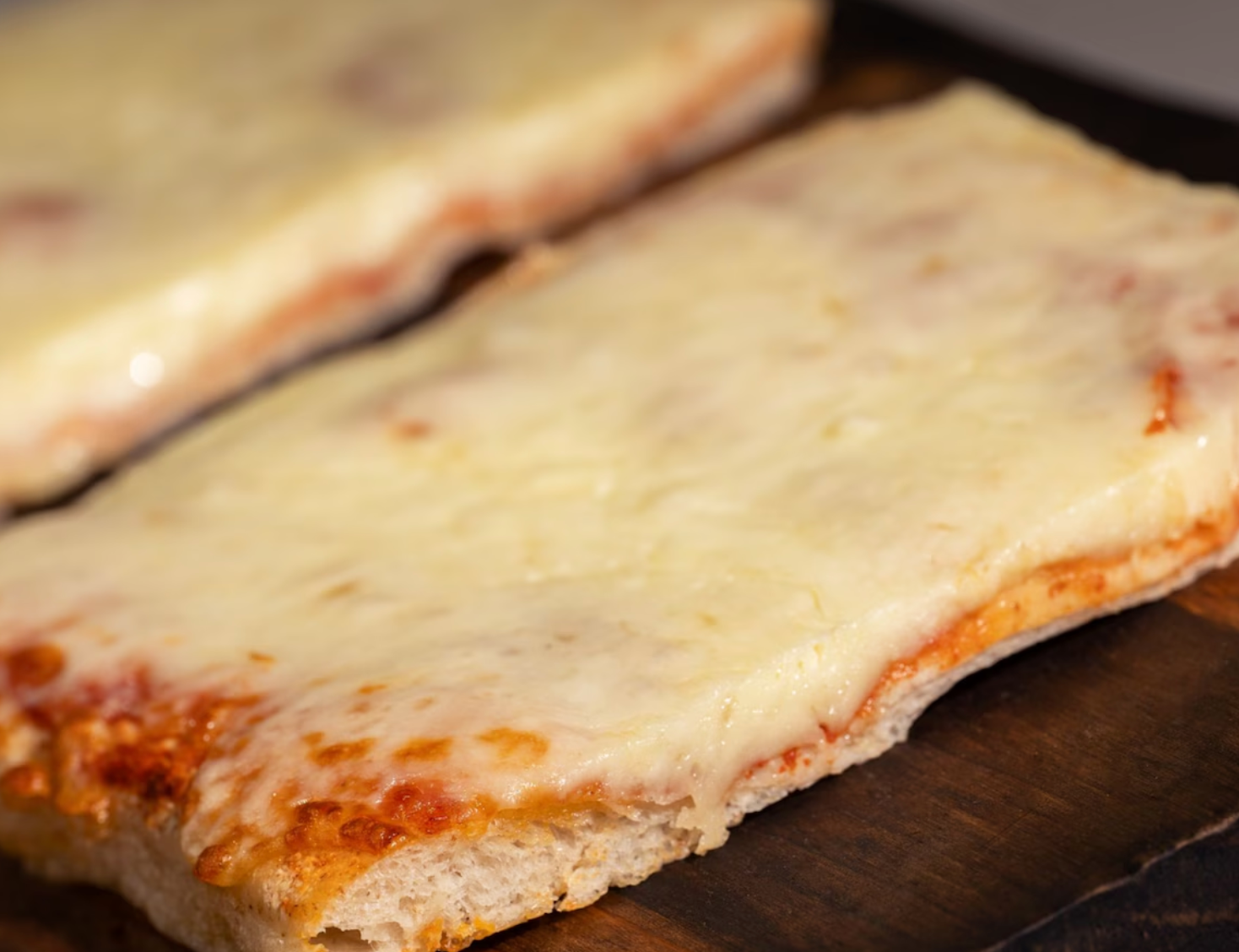 Close-up of cheese pizza with crispy crust on wooden surface.