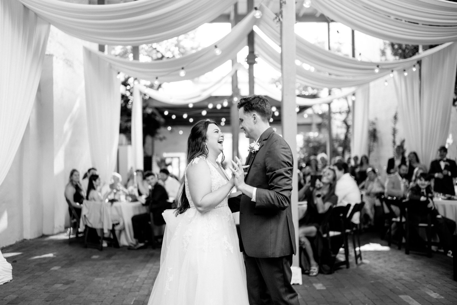 A bride in a flowing white ballgown twirls on a terracotta-tiled patio against white stucco walls.
