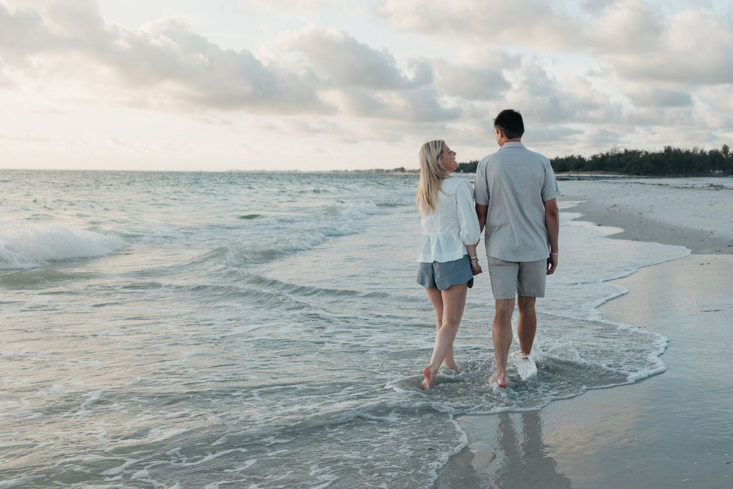 Two people strolling along a peaceful beach shoreline at sunset with gentle waves rolling in.