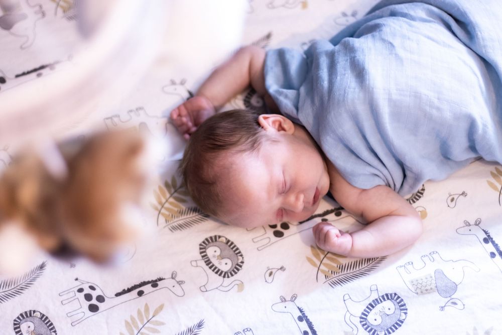 Infant sleeping on white blanket with animal print pattern.
