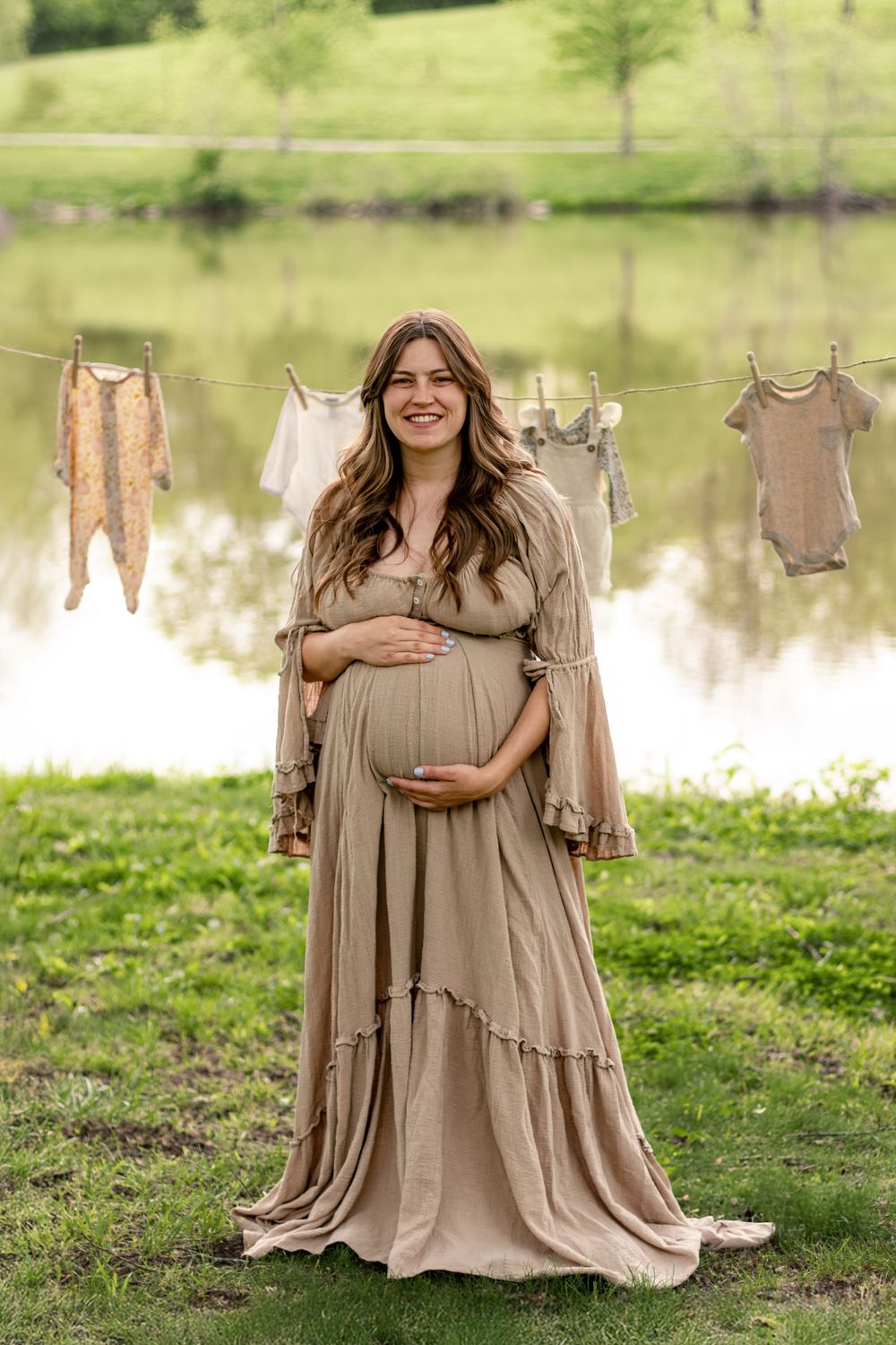 Maternity photoshoot featuring flowing tan dress against natural outdoor backdrop with pond.
