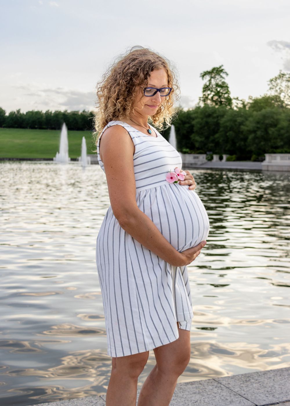 Maternity photo session by a pond with fountains at sunset.