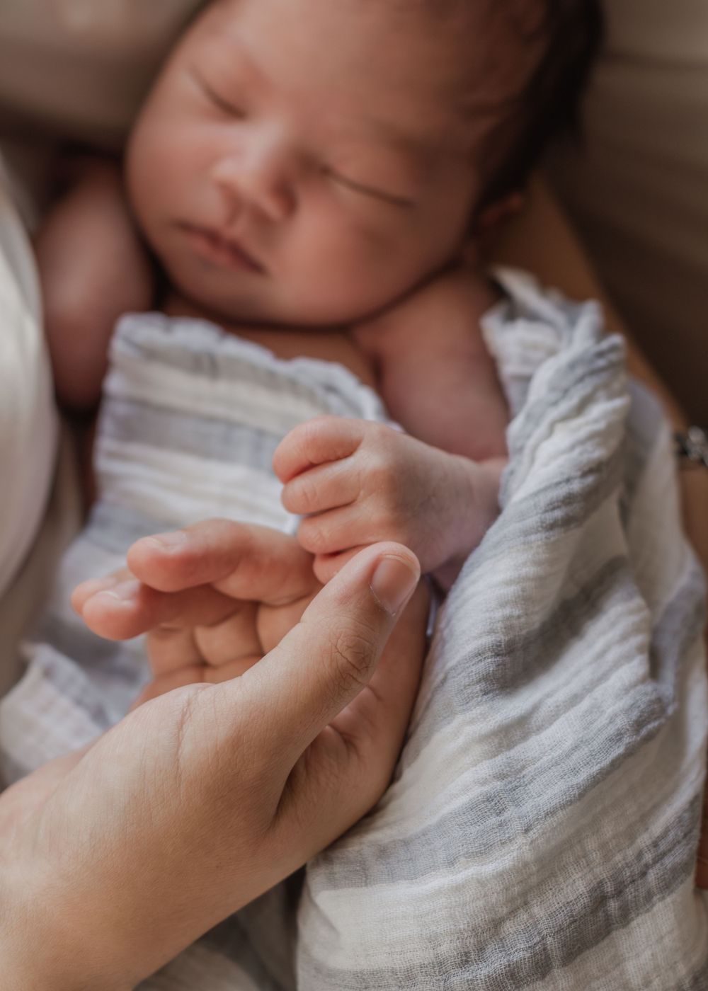 Peaceful sleeping newborn wrapped in textured white blanket with gentle hand touching.