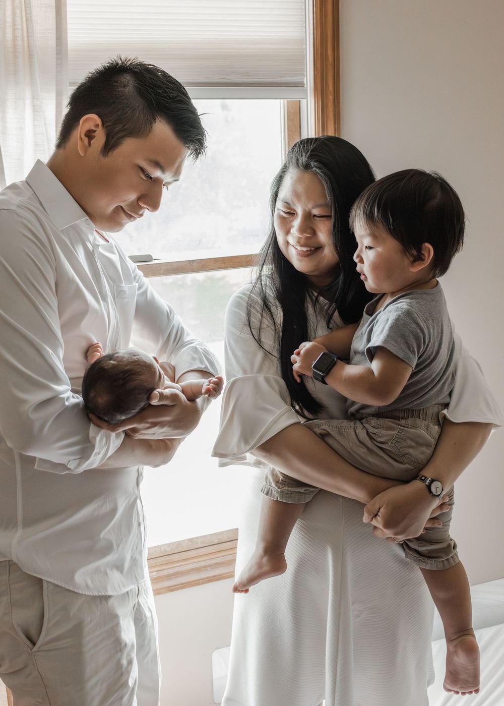 Candid family moments showing interaction with newborn by window.