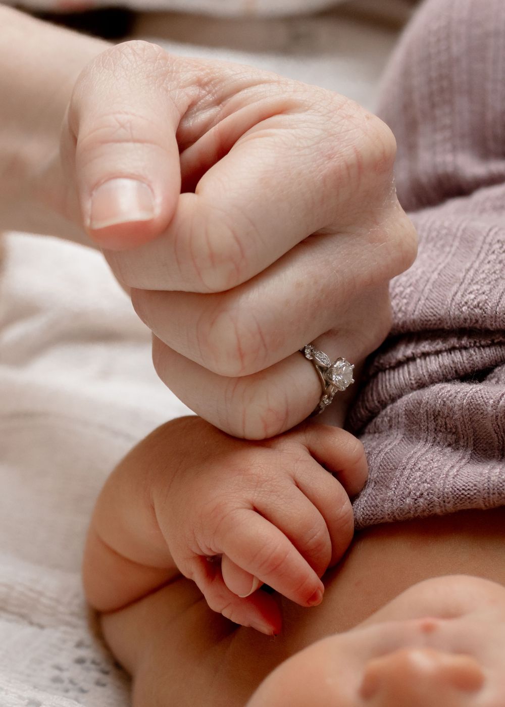 Detailed view of baby's small hand with delicate fingers resting on purple fabric.