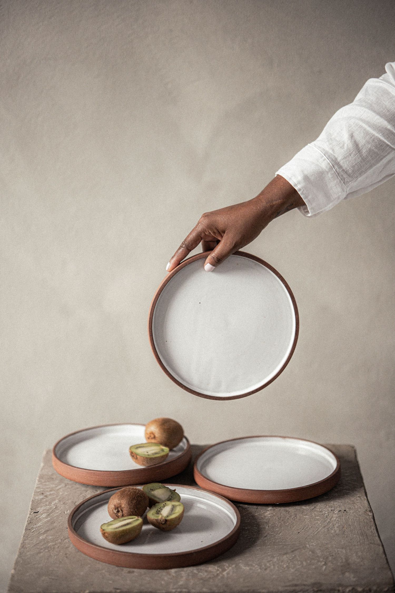 Hand holding ceramic plate above rustic table with kiwi fruits on plates.