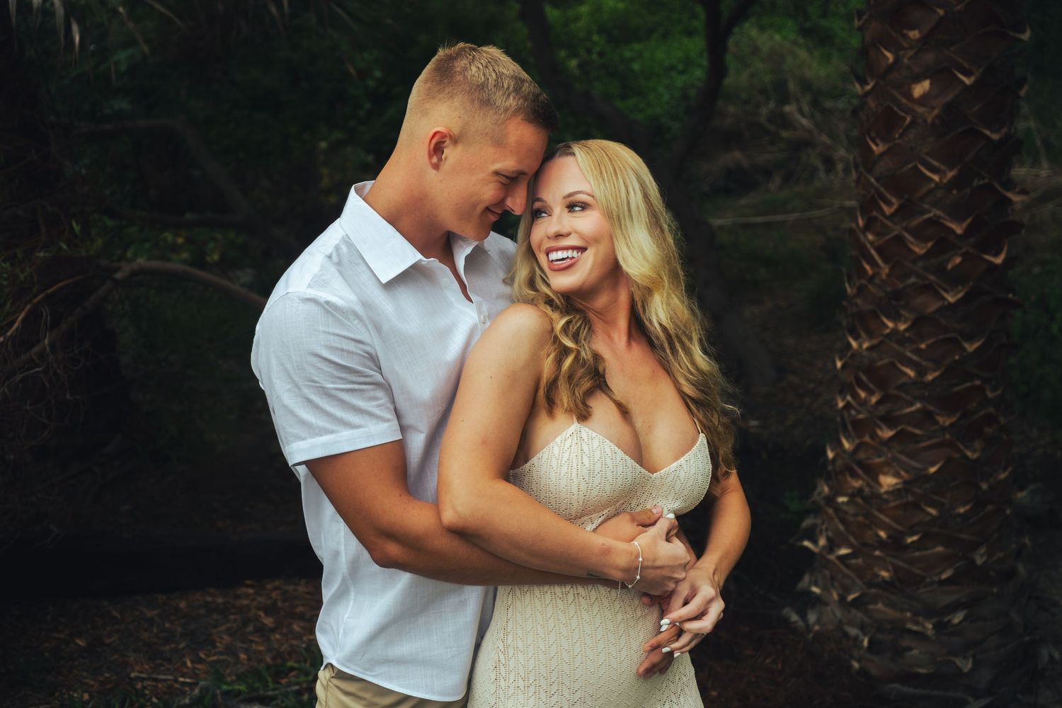 A romantic couple embraces outdoors near palm trees during a sunset photoshoot at table rock, laguna beach