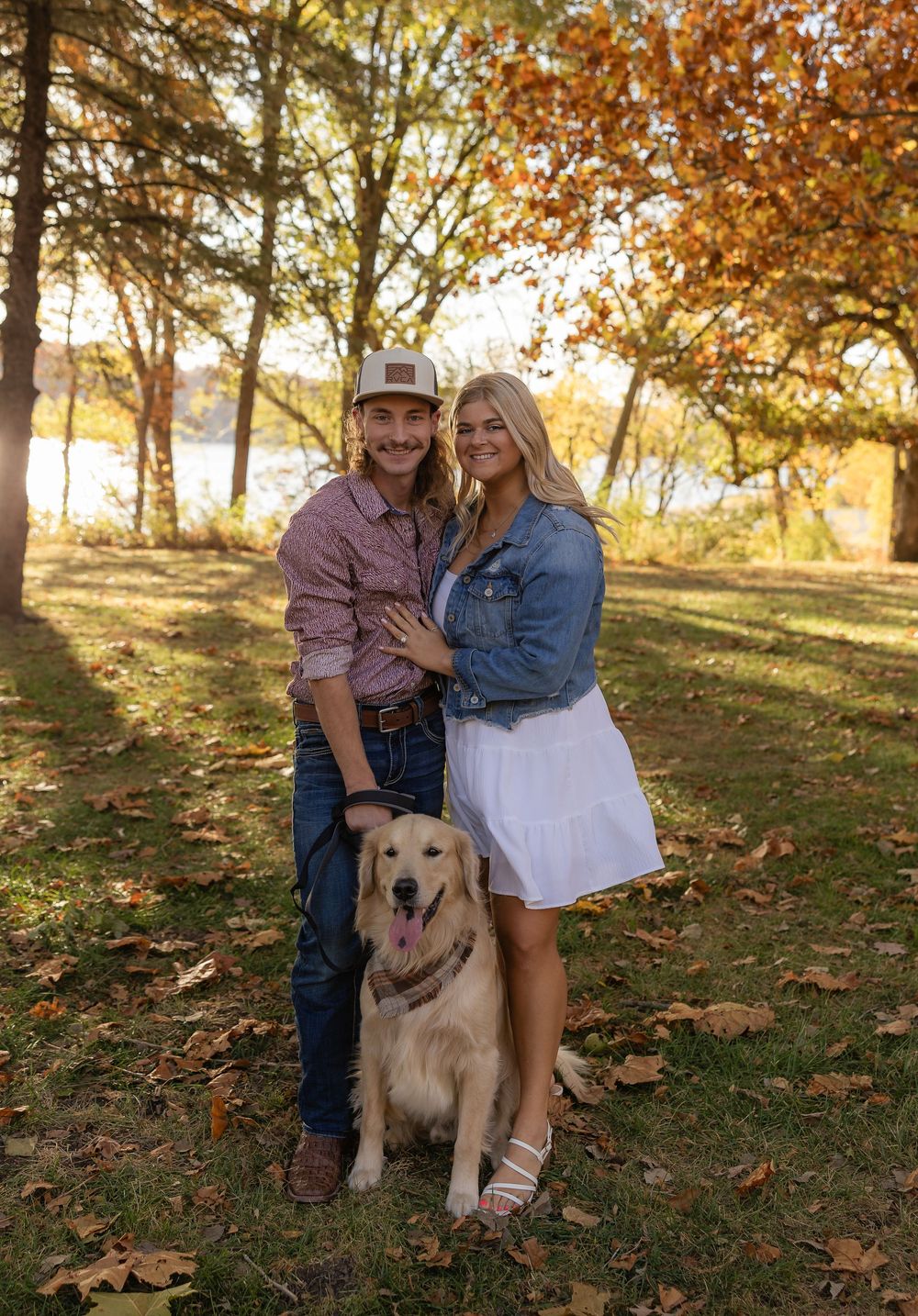 Golden retriever joins couple for outdoor autumn photoshoot among fallen leaves.