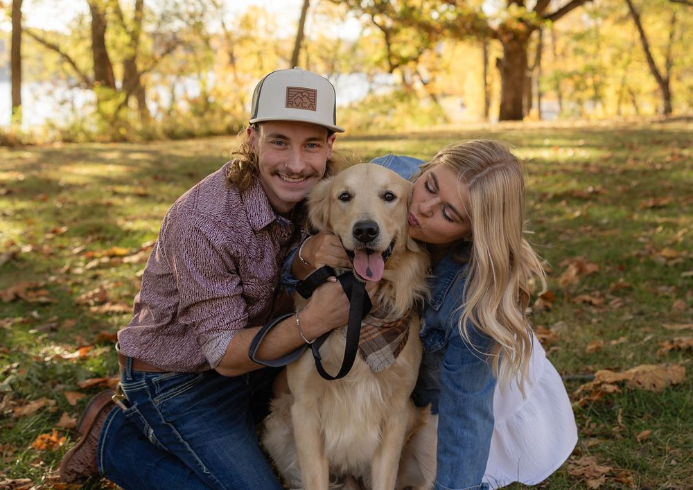 Happy couple cuddles with their golden retriever during fall photo session.
