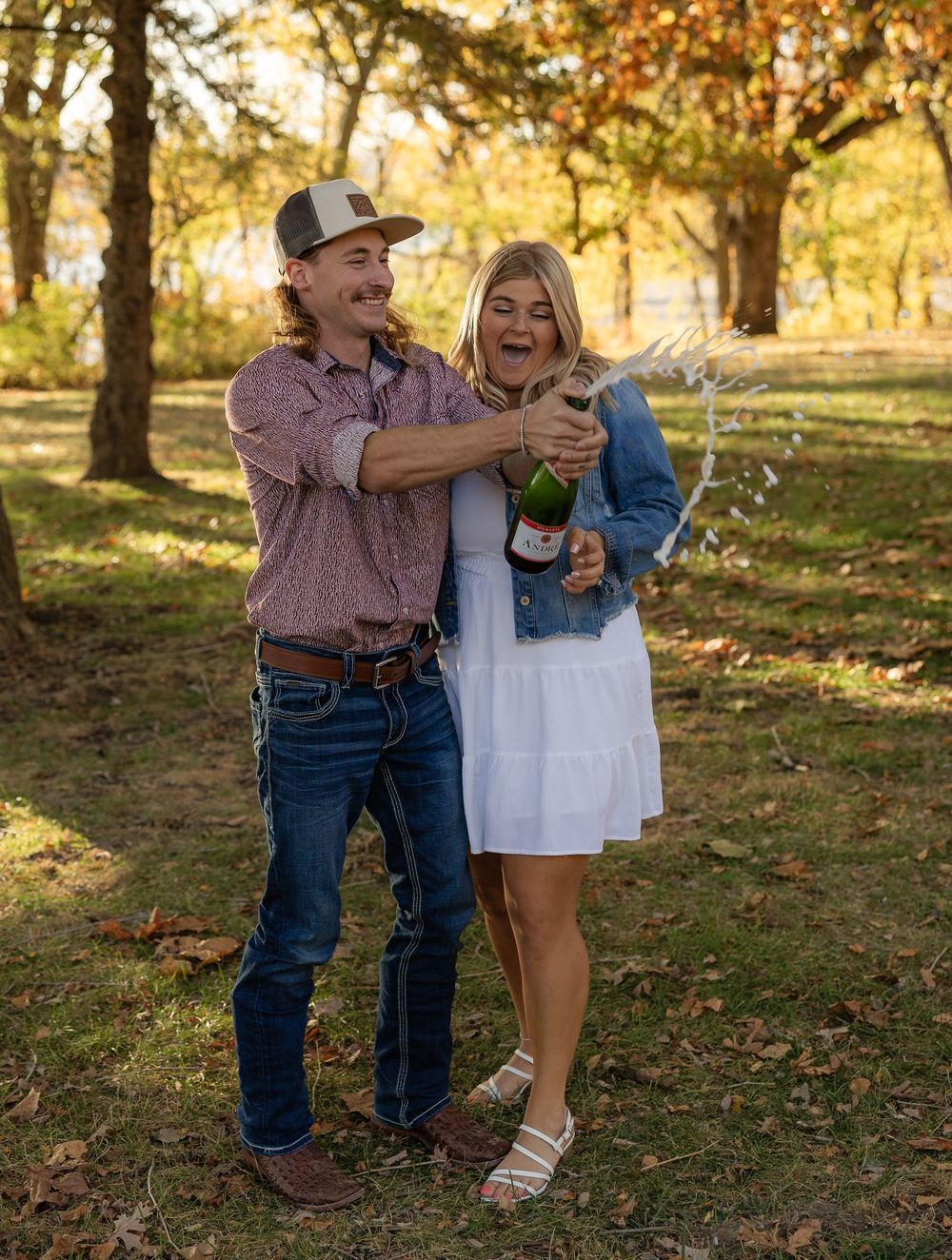 Couple celebrating with champagne in a fall forest setting.