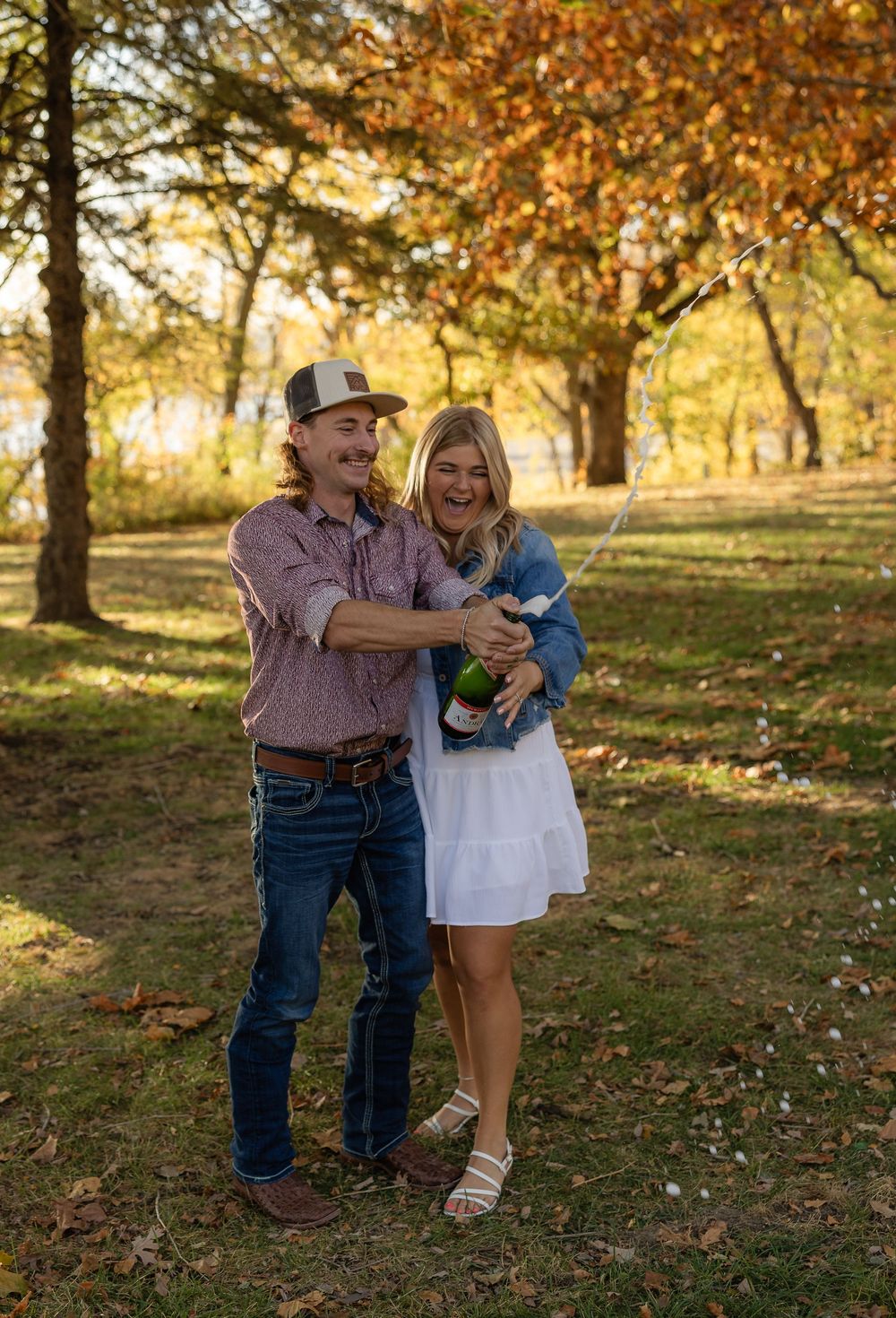 Couple popping champagne together in a golden-lit forest.