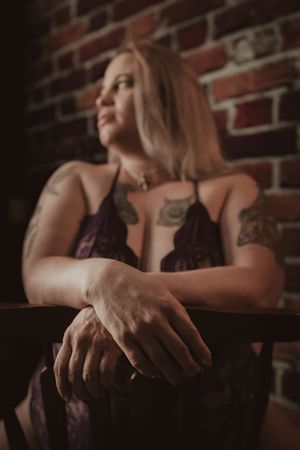 Artistic boudoir portrait of a person in black lace against a brick wall in moody lighting.