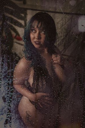 Artistic moody portrait through water-streaked glass with dark shadows and dramatic lighting effects.