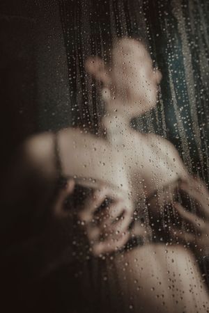 Silhouette behind wet glass with water droplets in moody atmospheric composition.