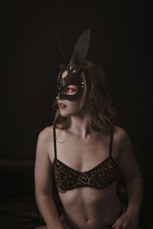 Artistic portrait of someone wearing a dark bunny mask and leopard print lingerie against a black background.