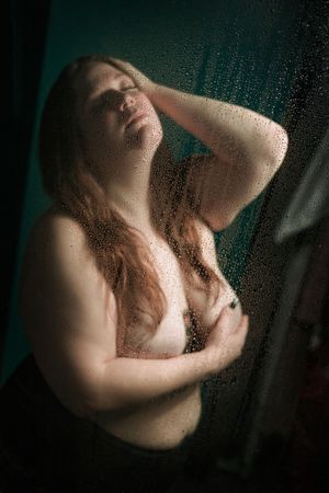 Artistic silhouette of a figure framed by a window, backlit against a dark moody background with water droplets visible.