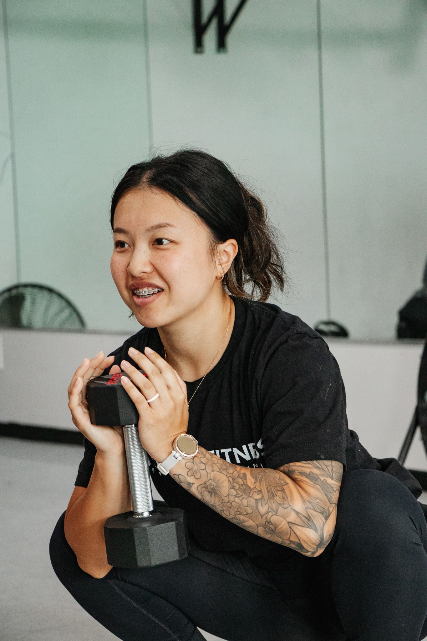 Woman with tattooed arm holding a dumbbell close to her chest while smiling during a workout